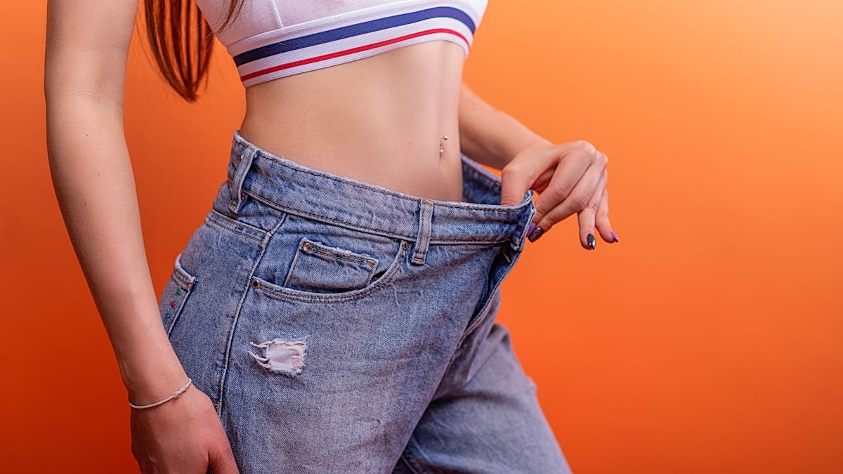 A woman holding loose jeans against her slim waist, symbolizing successful weight loss.